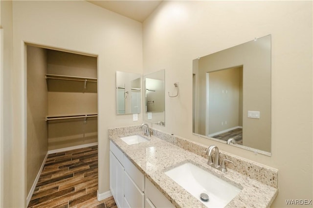 full bathroom featuring wood finish floors, a sink, baseboards, and double vanity