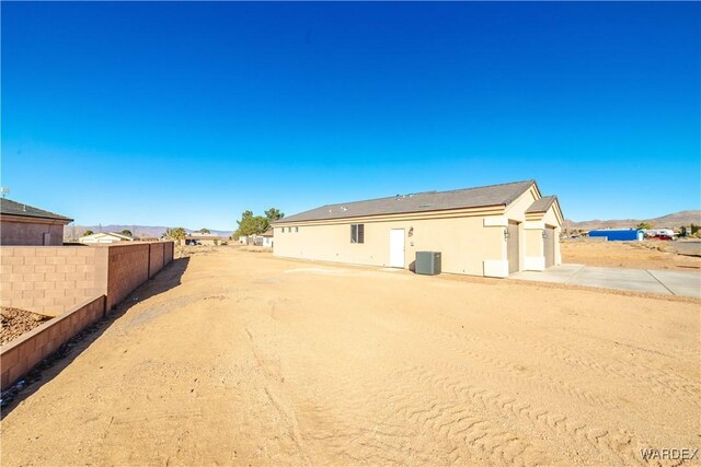 rear view of house featuring central AC unit, fence, and stucco siding