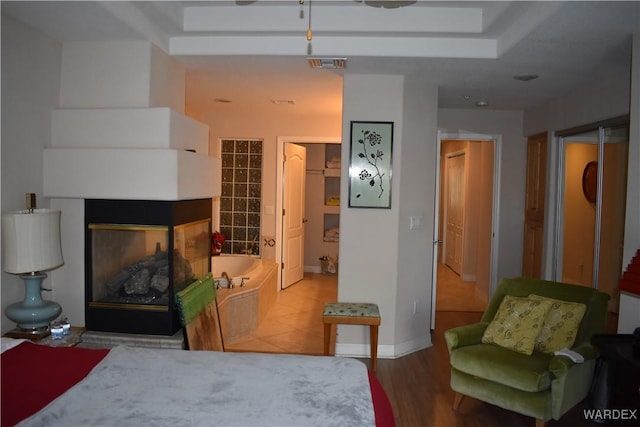 bedroom featuring baseboards, visible vents, light wood-style flooring, and a multi sided fireplace