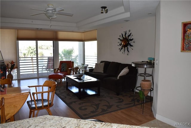 living room featuring a ceiling fan, a raised ceiling, and wood finished floors