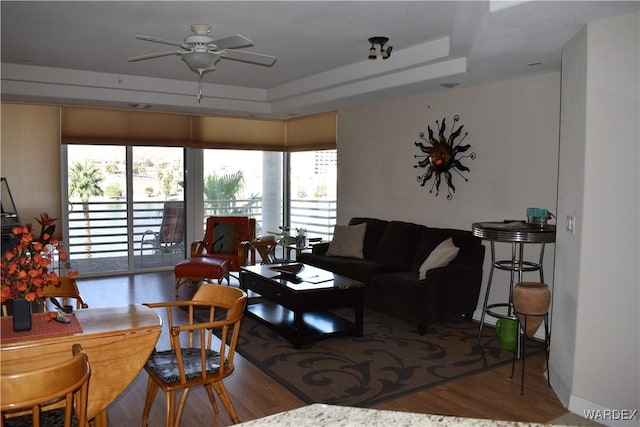 living room featuring a ceiling fan, a tray ceiling, and wood finished floors