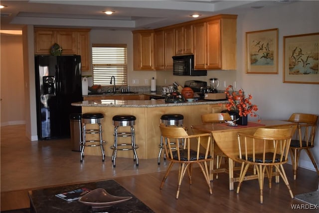 kitchen with stove, a kitchen breakfast bar, dark stone countertops, black fridge, and a sink