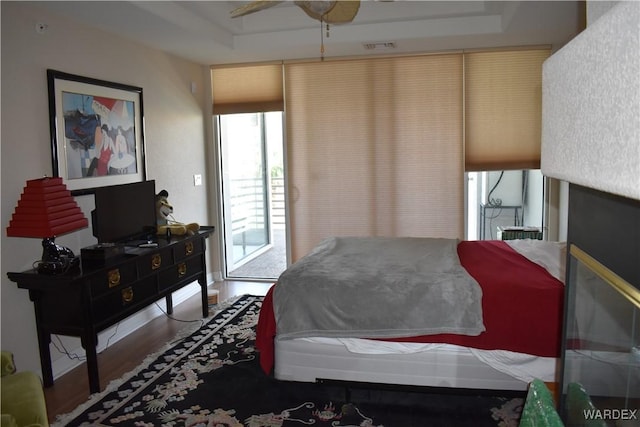 bedroom with a tray ceiling, access to outside, visible vents, and wood finished floors