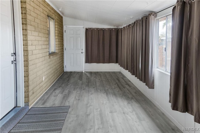 unfurnished room featuring light wood-type flooring, lofted ceiling, and brick wall