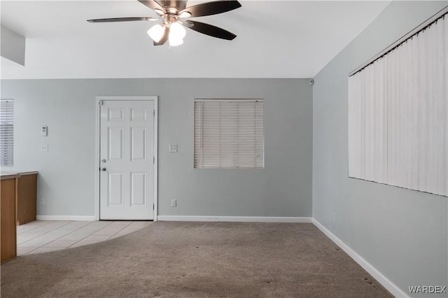 spare room with light carpet, light tile patterned floors, ceiling fan, and baseboards