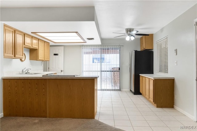 kitchen with light countertops, freestanding refrigerator, a sink, ceiling fan, and a peninsula