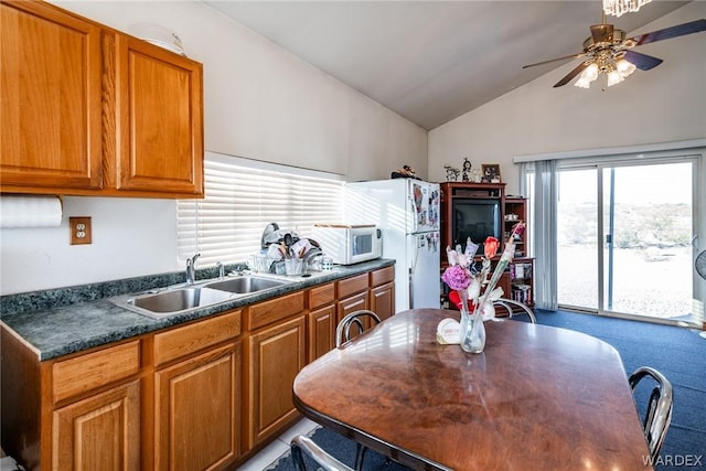 kitchen with brown cabinetry, dark countertops, white appliances, and a sink