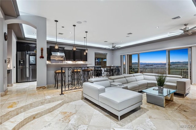 living area with visible vents, a ceiling fan, a tray ceiling, arched walkways, and baseboards