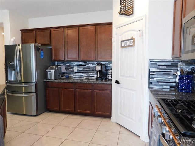 kitchen with decorative backsplash, stainless steel appliances, dark stone countertops, and light tile patterned flooring