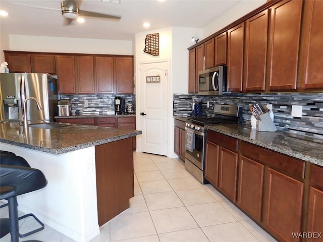 kitchen featuring dark stone counters, ceiling fan, stainless steel appliances, a kitchen bar, and light tile patterned flooring