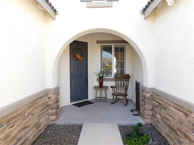 doorway to property with covered porch and stucco siding