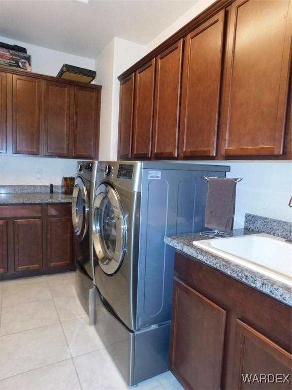 laundry area featuring cabinet space, light tile patterned floors, separate washer and dryer, and a sink