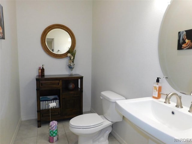 half bathroom with a sink, tile patterned flooring, toilet, and baseboards