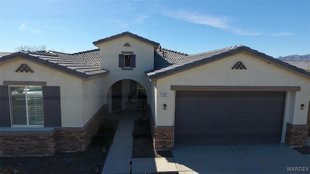 mediterranean / spanish house with driveway, stone siding, an attached garage, and stucco siding