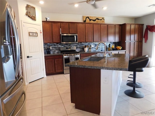 kitchen featuring light tile patterned flooring, stainless steel appliances, a sink, decorative backsplash, and an island with sink