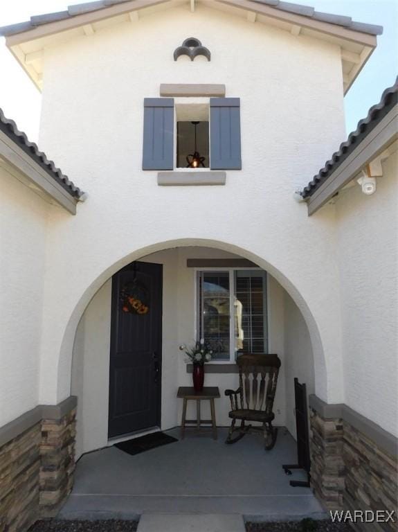 view of exterior entry with a porch, a tile roof, and stucco siding