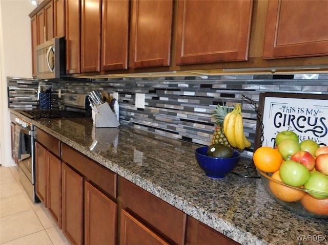 kitchen with stainless steel appliances, dark stone counters, decorative backsplash, and light tile patterned floors