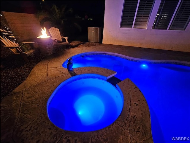 pool at night with a patio and a pool with connected hot tub