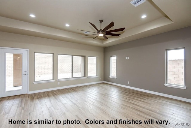 unfurnished room with light wood-style floors, a raised ceiling, visible vents, and baseboards