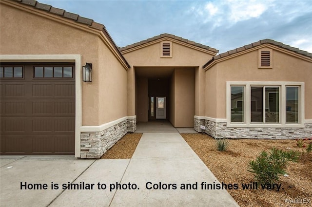 view of exterior entry with stone siding, an attached garage, a tiled roof, and stucco siding