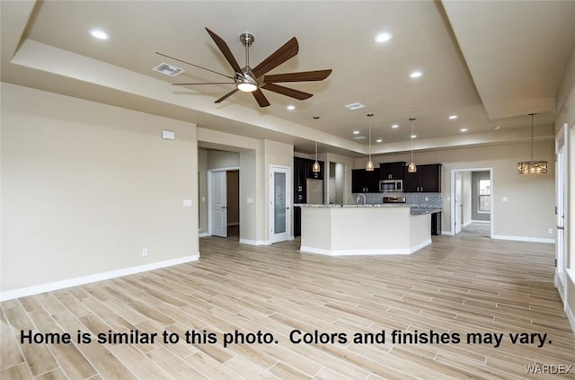 kitchen with stainless steel microwave, open floor plan, a tray ceiling, wood finish floors, and recessed lighting