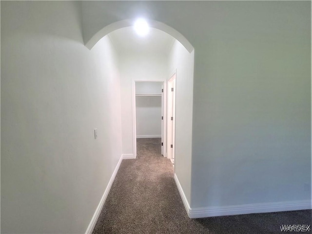 corridor featuring baseboards, arched walkways, and carpet flooring