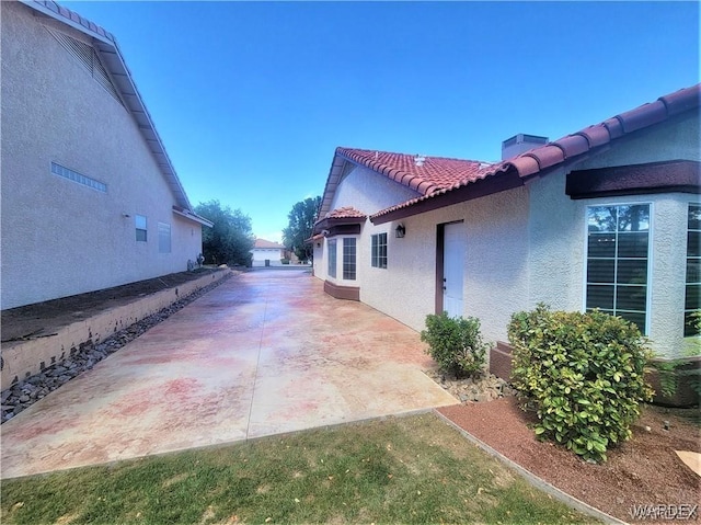 view of property exterior with a patio area, a tile roof, and stucco siding