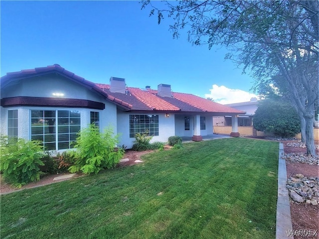 back of property featuring a chimney, a yard, a tiled roof, and stucco siding