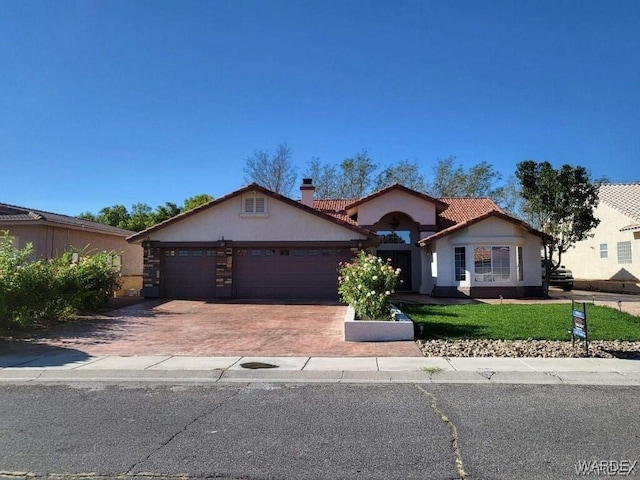 view of front of house with decorative driveway, a tile roof, stucco siding, a garage, and a front lawn