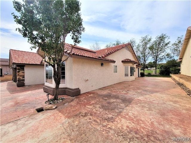 view of side of property with a patio area, a tile roof, and stucco siding