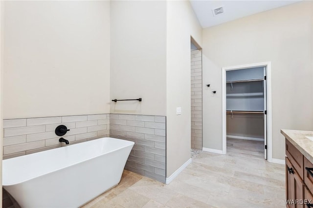 full bathroom with a freestanding tub, visible vents, vanity, tile walls, and a spacious closet