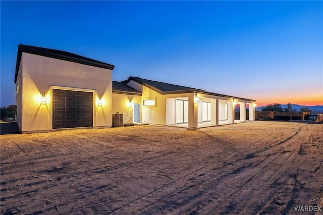 back of property at dusk featuring central AC unit, an attached garage, and stucco siding