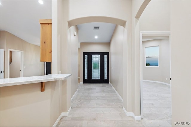 foyer featuring arched walkways, a wealth of natural light, visible vents, and baseboards