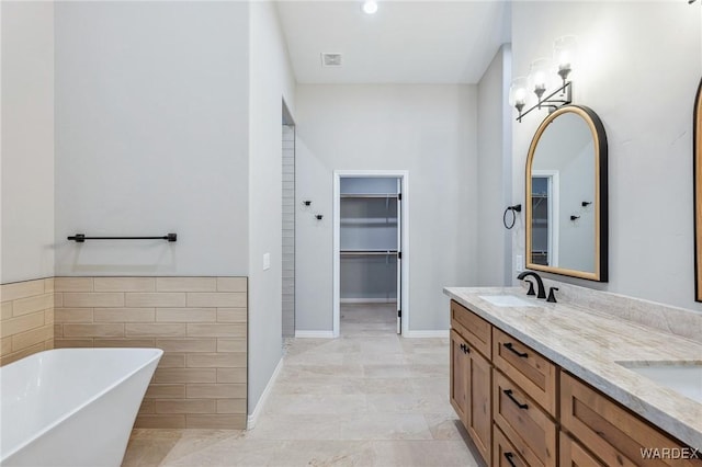 full bathroom with a walk in closet, tile walls, double vanity, a sink, and a freestanding tub