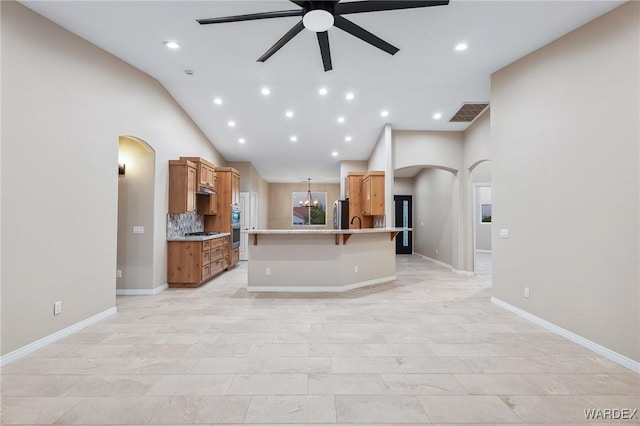 kitchen featuring arched walkways, brown cabinets, a breakfast bar area, and ceiling fan with notable chandelier