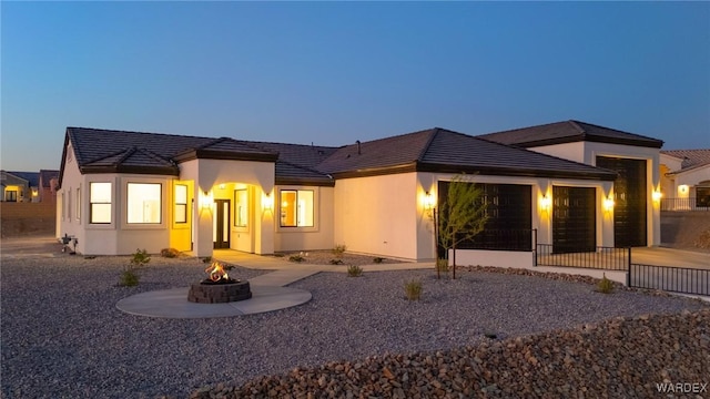 back of property with a garage, an outdoor fire pit, and stucco siding