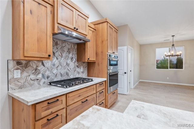 kitchen with light stone counters, a notable chandelier, stainless steel appliances, hanging light fixtures, and under cabinet range hood