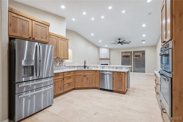 kitchen featuring stainless steel appliances, light countertops, brown cabinetry, a sink, and a peninsula