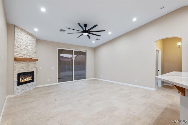 unfurnished living room featuring arched walkways, a fireplace, visible vents, ceiling fan, and baseboards