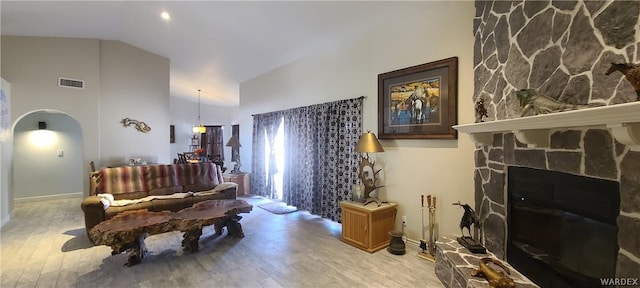 living area with arched walkways, a stone fireplace, light wood finished floors, and visible vents