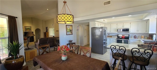 dining room with arched walkways, vaulted ceiling, a raised ceiling, and visible vents