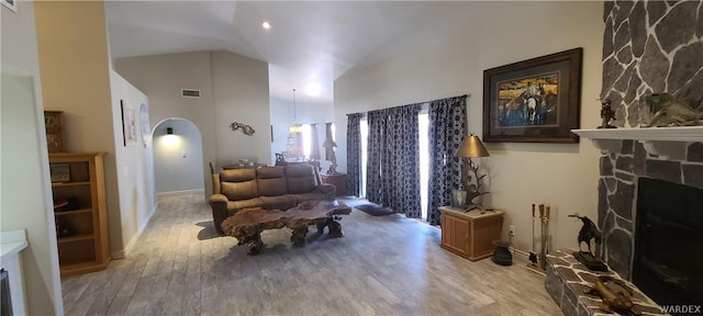 living area with arched walkways, high vaulted ceiling, light wood-style flooring, a fireplace, and visible vents