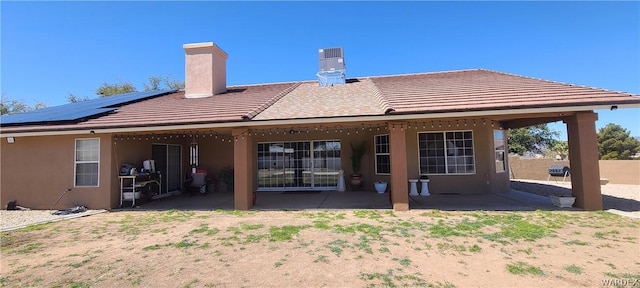 rear view of house featuring solar panels, a patio, a chimney, and stucco siding