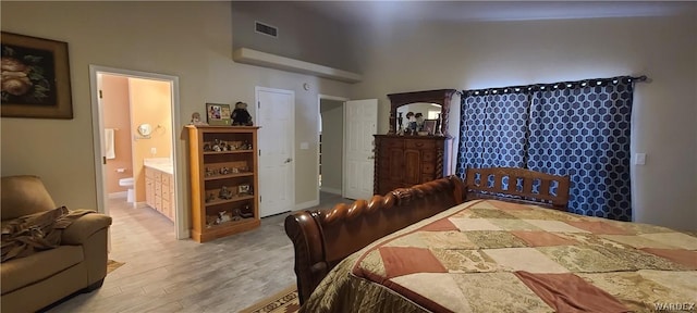 bedroom with high vaulted ceiling, wood finished floors, visible vents, baseboards, and ensuite bath