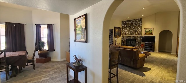 living area with lofted ceiling, arched walkways, wood finished floors, and a stone fireplace