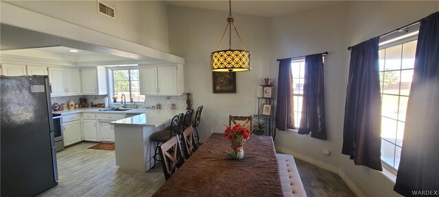 kitchen with decorative light fixtures, freestanding refrigerator, white cabinets, a peninsula, and a kitchen breakfast bar