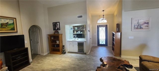 foyer featuring baseboards, visible vents, arched walkways, wood finished floors, and a high ceiling