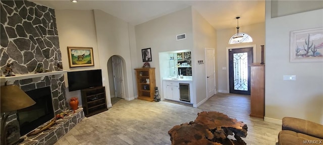 entryway with arched walkways, a fireplace, visible vents, a towering ceiling, and light wood-type flooring