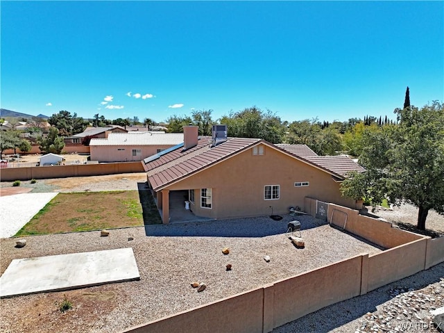 view of property exterior featuring a chimney, stucco siding, a patio area, a fenced backyard, and a tiled roof