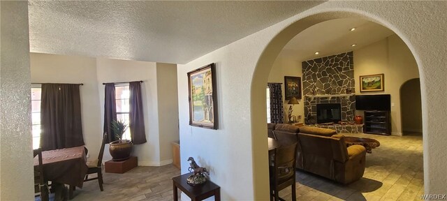 living area featuring lofted ceiling, arched walkways, wood finished floors, and a textured wall